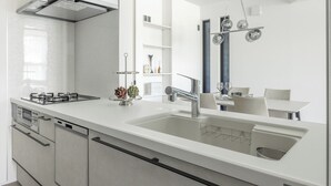 A modern kitchen with a white countertop, stainless steel appliances, and a dining area with a table and chairs. - Charm Roger luxury room Bridge (Kamakura)