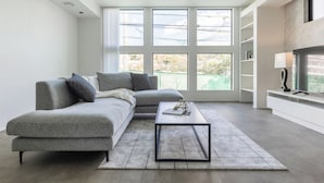 A modern living room with a grey sofa, a coffee table, and a large window with a view of greenery. - Charm Roger luxury room Bridge (Kamakura)