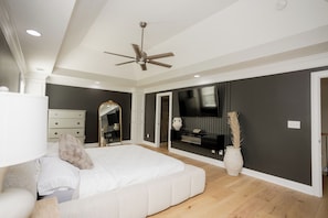 Une chambre à coucher comprenant un lit, un ventilateur de plafond, une commode, un miroir, un téléviseur et un vase avec des plantes.