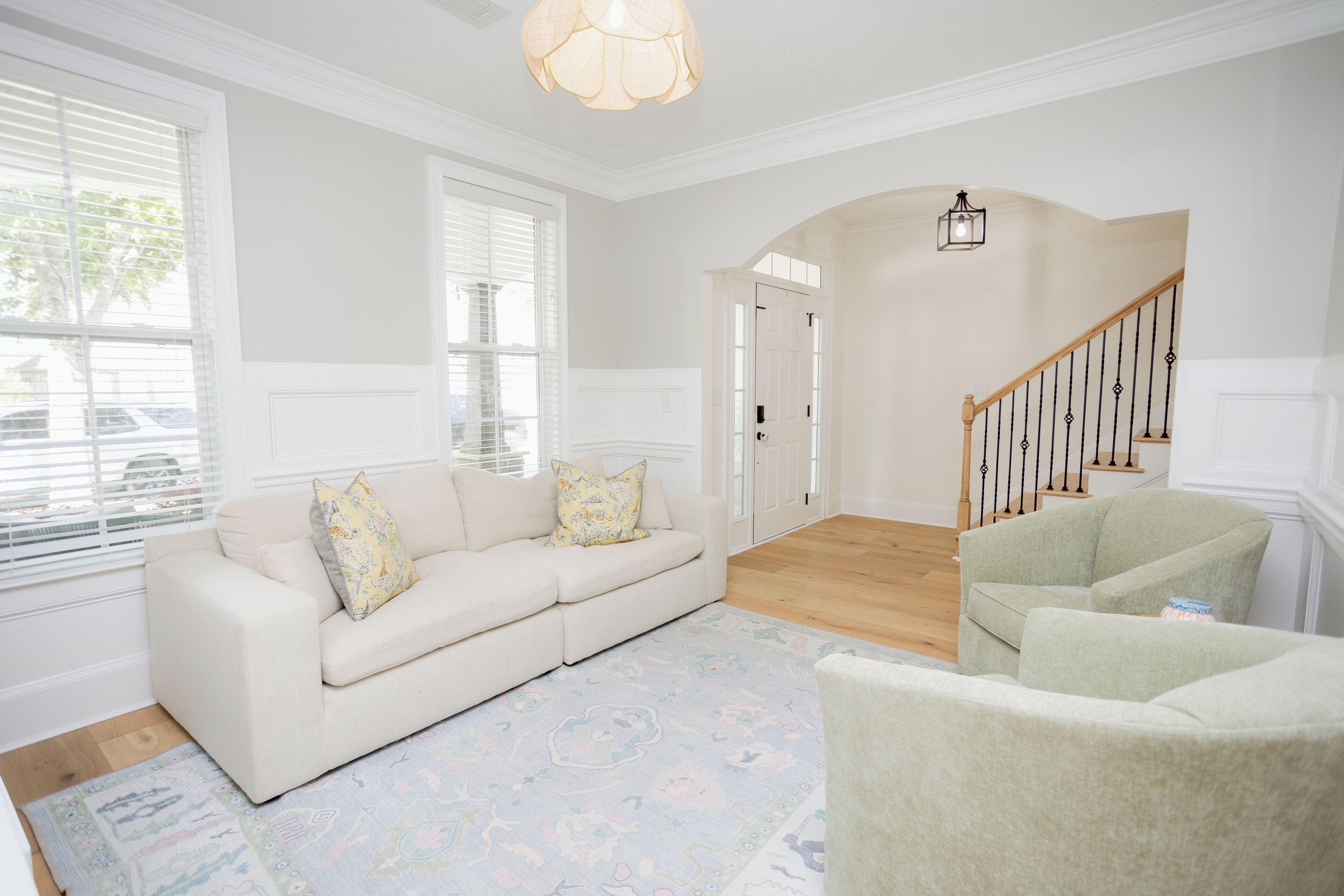 A living room with a sofa, armchairs, a patterned rug, a staircase, and a door leading to another room.