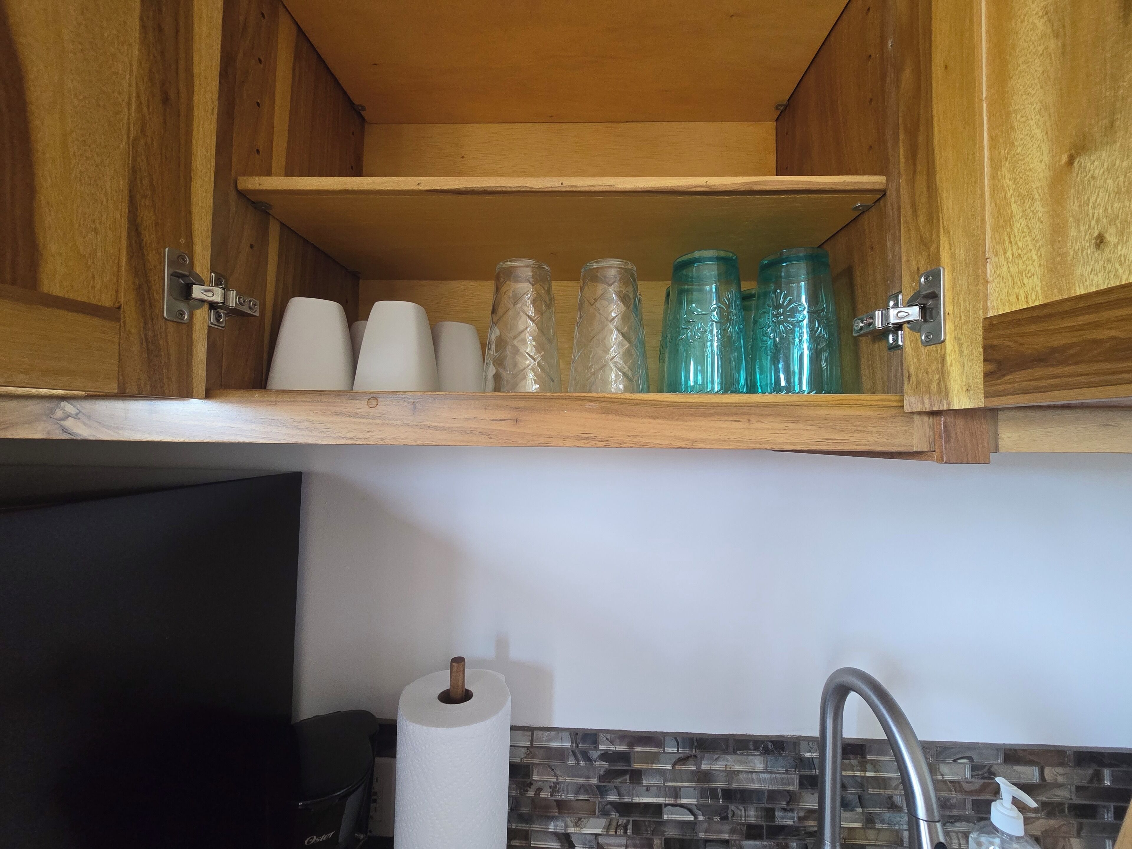 A kitchen with wooden cabinets, a shelf with glass jars, a roll of paper towels, and a faucet.