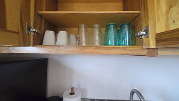 A kitchen with wooden cabinets, a shelf with glass jars, a roll of paper towels, and a faucet.