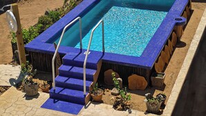 Una piscina cuadrada con escalones de azulejos azules y una cubierta de madera alrededor.