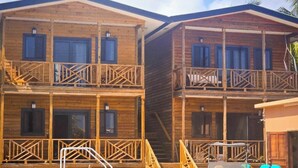 Una cabaña de madera con balcón, zona de piscina y un espacio de estar al aire libre cubierto.