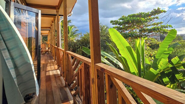Una terraza de madera con barandilla, vistas a exuberante follaje y un cielo despejado.