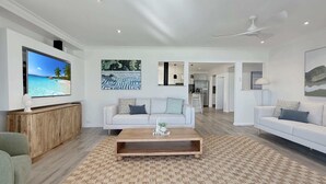 Ein modernes Wohnzimmer mit einem Flachbildfernseher, einem Holztisch, zwei weißen Sofas und einem gemusterten Teppich.