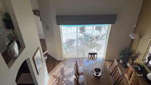 A dining area with a wooden table, chairs, a vase, and a large window with a view of outdoor furniture. - Magical Disney Retreat w/Private Heated Pool/Hot Tub - Spacious 5-bedroom (Kissimmee)