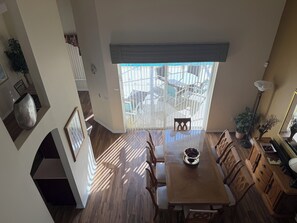 A dining area with a wooden table, chairs, a vase, and a large window with a view of outdoor furniture. - Magical Disney Retreat w/Private Heated Pool/Hot Tub - Spacious 5-bedroom (Kissimmee)