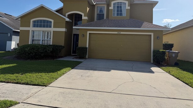 A residential house with a garage, a driveway, and a well-maintained lawn. - Magical Disney Retreat w/Private Heated Pool/Hot Tub - Spacious 5-bedroom (Kissimmee)