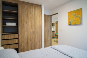 Een slaapkamer met een grote houten garderobe, een bed met een witte dekbedovertrek, en een schilderij aan de muur.