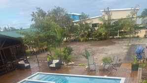 Un terrazzo in legno con una piscina rettangolare, circondato da piante in vaso e mobili da esterno.