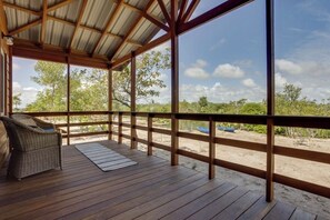 A covered outdoor deck with a wicker chair, wooden railings, and a view of the beach and trees. - Tortuga Amarilla 1 & 2 make up this great multi building hideaway in Maya Beach (Maya Beach)