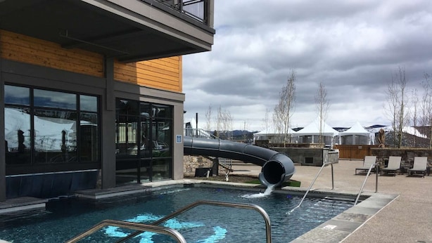 Ein Schwimmbad mit Wasserrutsche, eine Liegefläche mit Stühlen und ein Gebäude mit großen Fenstern.