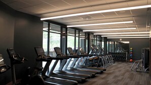 Ein Fitnessraum mit mehreren Laufbändern, großen Fenstern und verschiedenen Gewichten sowie Übungsbällen.