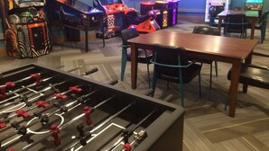 Ein Spielzimmer mit mehreren Arcade-Automaten, einem Tischkicker und einigen Stühlen.