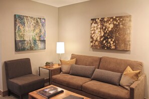 Un salon comprenant un canapé, un fauteuil, une table basse, une lampe et deux tableaux abstraits accrochés aux murs.