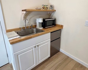 Cocina compacta con lavamanos, cafetera, microondas y un estante con frascos.