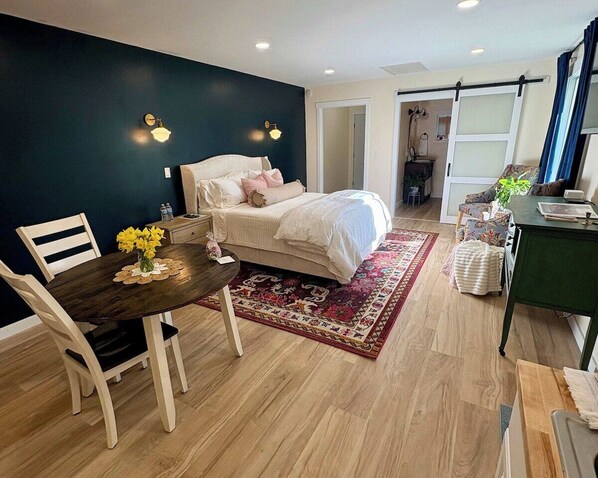 A bedroom with a bed, bedside tables, a desk, a chair, and a dining table.