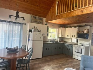 A cabin-style kitchen with a dining area, wooden ceiling, and a welcome sign.