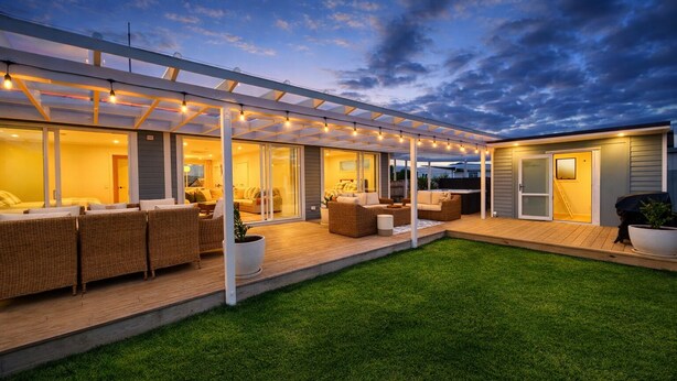 A modern outdoor living area with a covered patio, seating, and a well-maintained lawn.