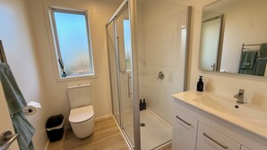 A modern bathroom with a glass shower enclosure, a toilet, a sink with a mirror, and a window providing natural light.