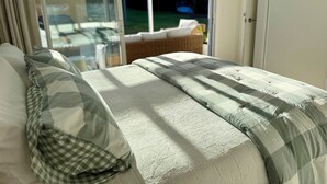 A bedroom with a bed, a checkered pillow, a window with a view of a garden, and a sliding glass door.
