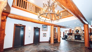 A spacious lobby with a stone floor, wooden columns, a chandelier, and a fireplace. - Spectacular Ski-in/Ski-out Mountain Condo with A/C! (Fernie)