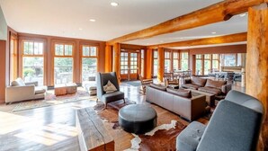 A spacious living area with large windows, a wooden ceiling, and a mix of seating arrangements. - Spectacular Ski-in/Ski-out Mountain Condo with A/C! (Fernie)