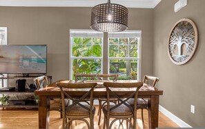 A dining area with a wooden table and chairs, a chandelier, a television, and a window with a view of greenery. - Cozy 4bdr House Gated Community Near Disney - 1105 (Kissimmee)