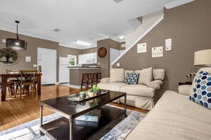 A living room with a sofa, coffee table, and a dining area with a table and chairs. - Cozy 4bdr House Gated Community Near Disney - 1105 (Kissimmee)