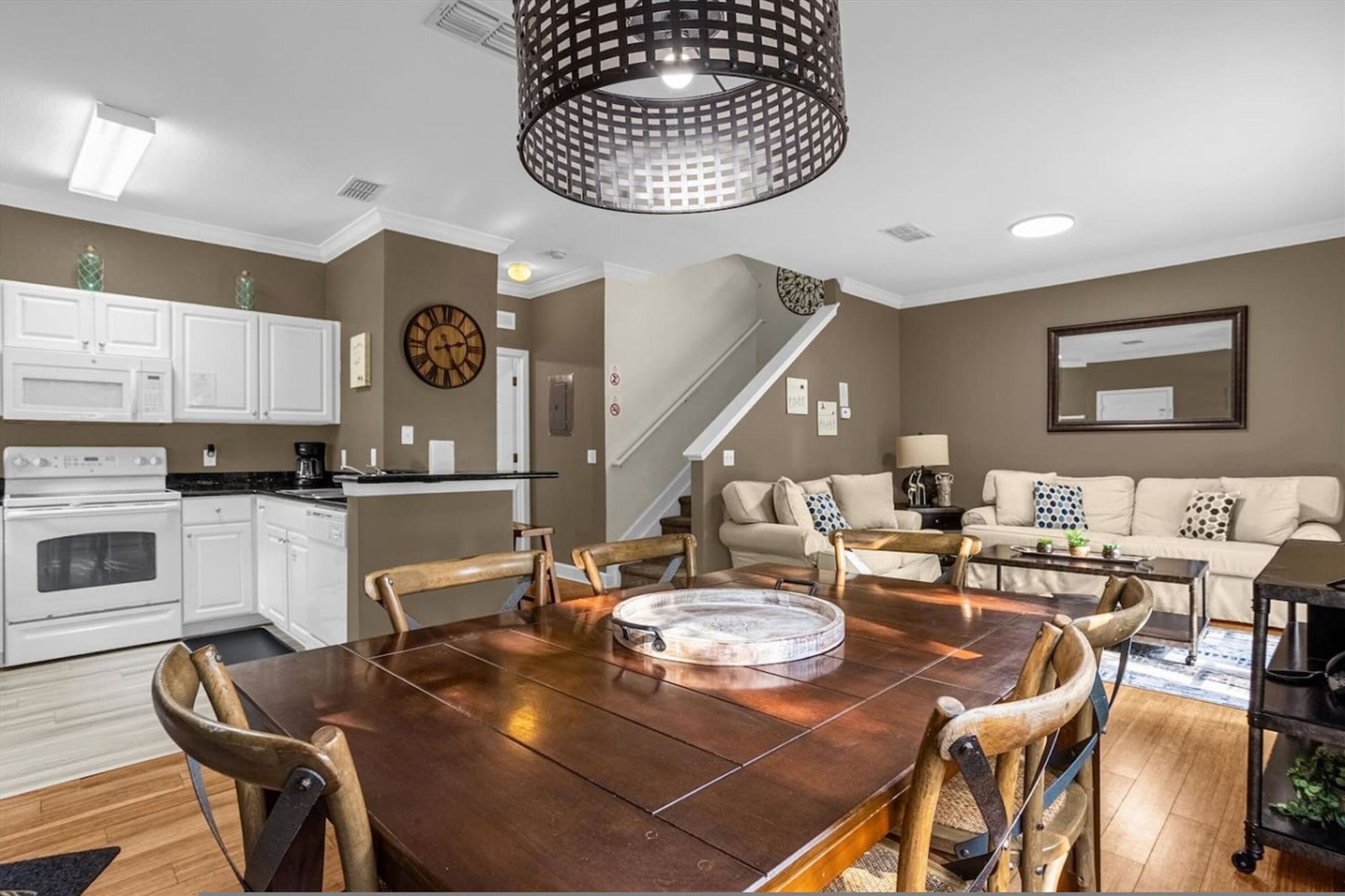 A dining area with a wooden table and chairs, a kitchen with white cabinets, and a staircase.