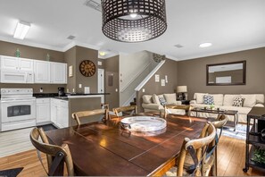 A dining area with a wooden table and chairs, a kitchen with white cabinets, and a staircase. - Cozy 4bdr House Gated Community Near Disney - 1105 (Kissimmee)
