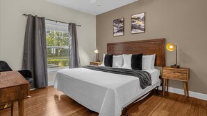 Quarto com uma cama grande, um ventilador de teto, duas mesas de cabeceira com luminárias, uma janela com cortinas e duas quadros na parede.