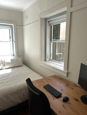Quarto com uma cama, uma escrivaninha com computador e uma janela.