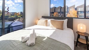 Une chambre d’hôtel avec un grand lit, une table de chevet avec une lampe et une vue sur les bâtiments par la fenêtre.