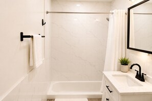 A modern bathroom with a bathtub, a shower, a sink with a mirror, and a towel rack. - Stunning 3BD Duplex with Private Garden Oasis (New York)