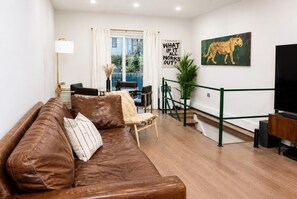 Ein Wohnzimmer mit brauner Ledersofa, einem Esstisch mit Stühlen, einem Fernseher und einem Gemälde einer Giraffe.