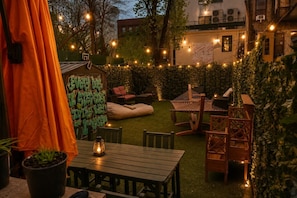A cozy outdoor patio with a wooden table and chairs, a hammock, and string lights. - Stunning 3BD Duplex with Private Garden Oasis (New York)