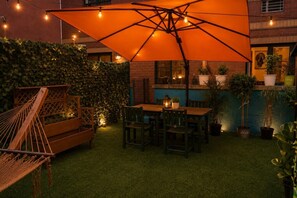 A patio with a wooden table and chairs, an orange umbrella, and a hammock. - Stunning 3BD Duplex with Private Garden Oasis (New York)