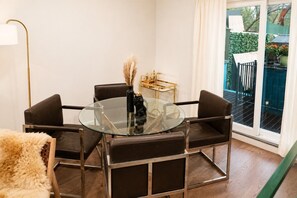 Et moderne spiseområde med et glasbord, sorte læderstole, et guldsidebord og en dekorativ vase med pampasgræs.