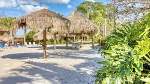 A beach with thatched-roof structures, a sandy area with lounge chairs, and lush greenery. - 3-bedroom 2BA condo near Disney! In a private resort! With beach! Pools!Hot tub! (Davenport)