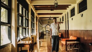 A corridor with wooden floors, a person carrying a tray, and tables and chairs along the sides. - Gimanhala Hotel (Dambulla)