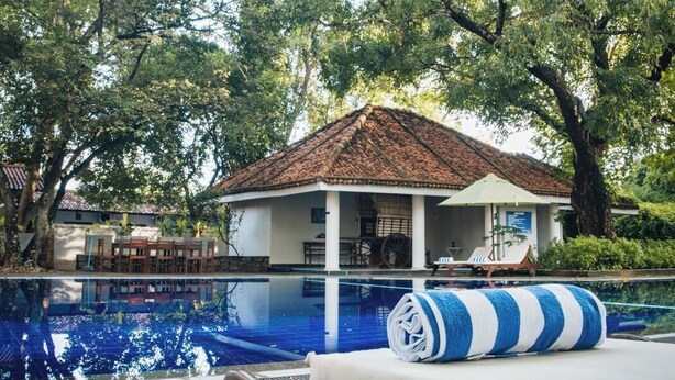 A pool area with a lounge chair, a small pavilion, and a tree-lined background. - Gimanhala Hotel (Dambulla)