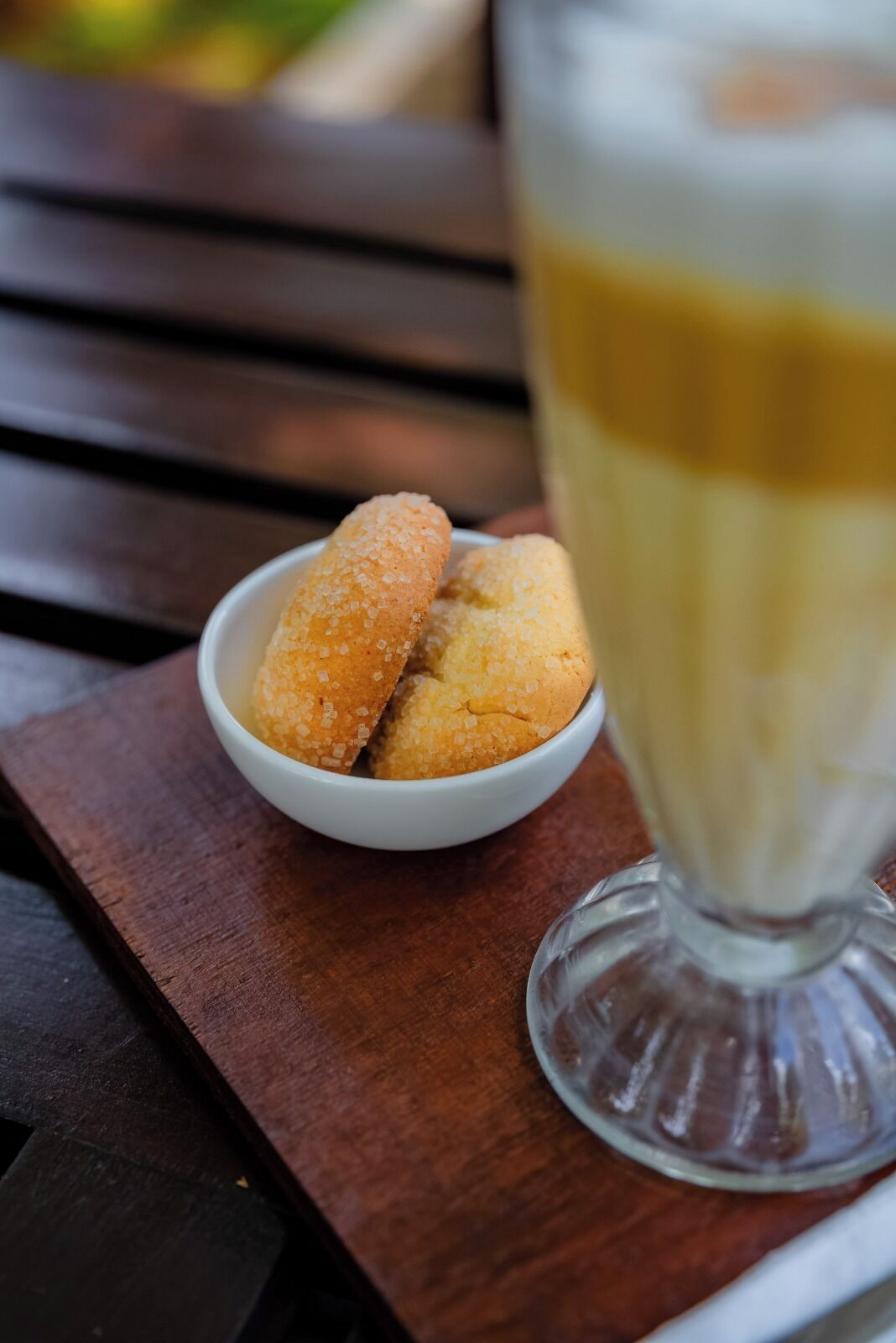 A wooden table with a white bowl containing two sugar-coated pastries and a glass of a light-colored beverage.