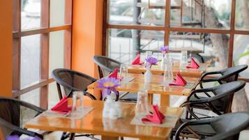 A row of wooden tables with chairs, each table set with a clear glass, a pink napkin, and a purple flower.