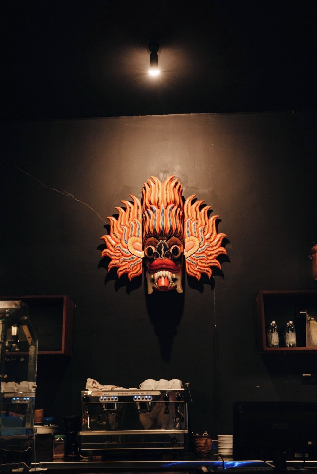 Un masque décoratif fixé au mur, avec une source de lumière centrale placée au-dessus.