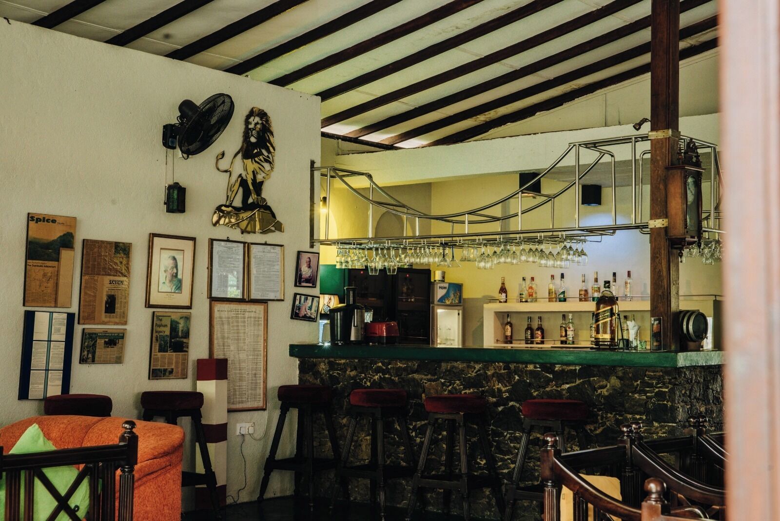 A bar area with stools, a counter with bottles, and a fan on the wall.