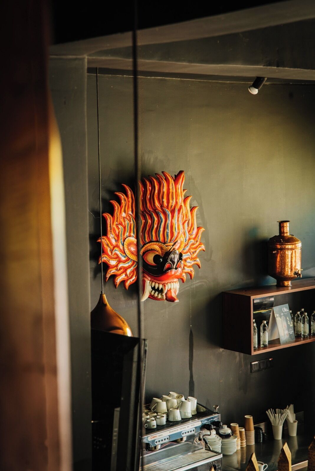 Una habitación con un detalle decorativo en la pared, una cafetera y una estantería con diversos objetos.