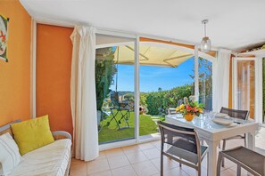 A room with a bed, a dining table with chairs, a sliding glass door leading to a garden, and a ceiling fan. - 1 bedroom apt - Sea View & Pool, Roquebrune-Sur-Argens, France (Roquebrune-Sur-Argens)