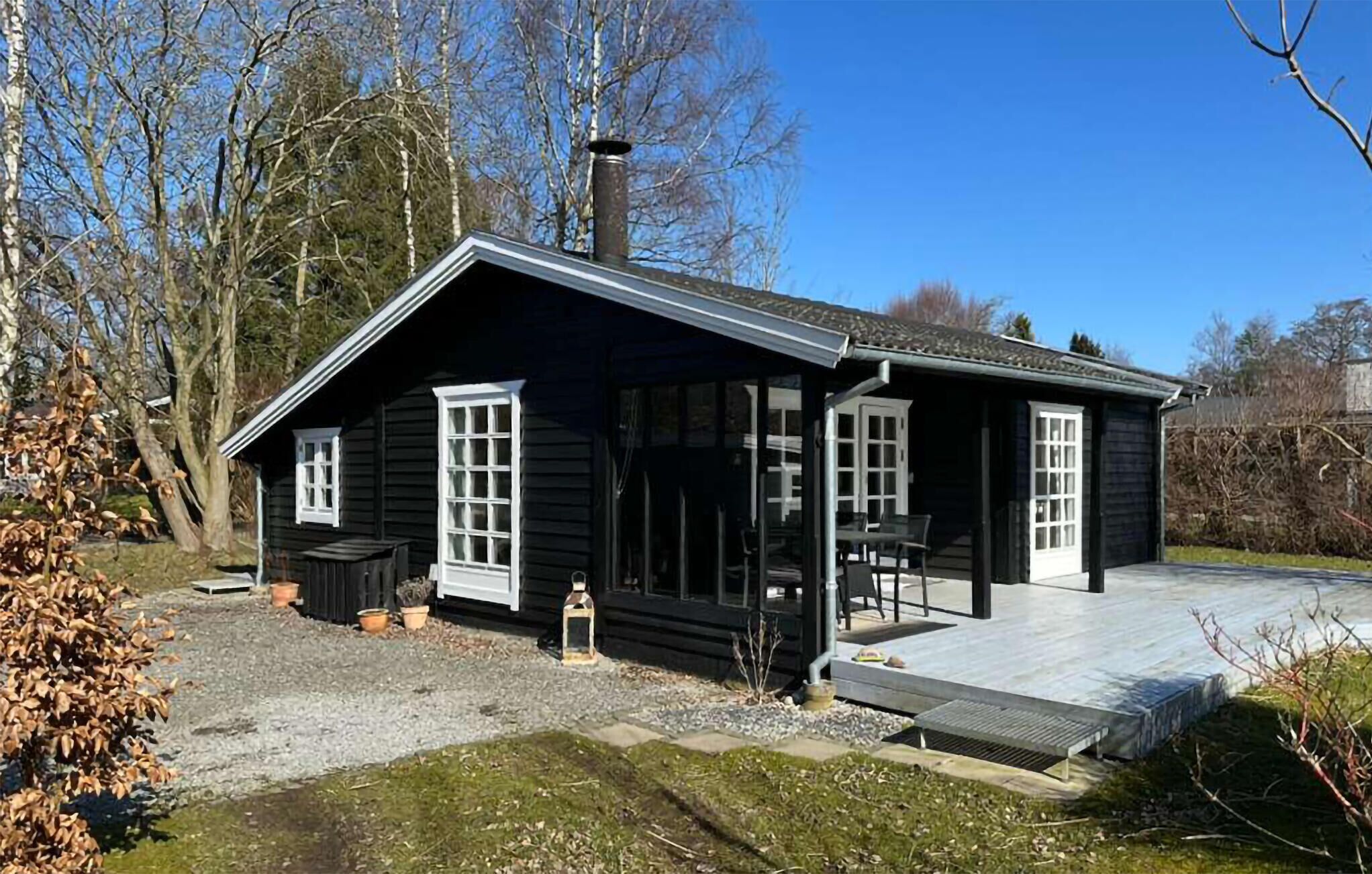 Een zwart houten gebouw met een veranda, schoorsteen en een klein tafeltje en stoel.